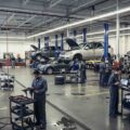 Auto dealership service department with multiple vehicles raised on lifts and technicians performing service and repair work.